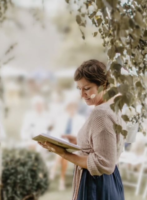 Frau liest im Freien aus einem Buch vor.