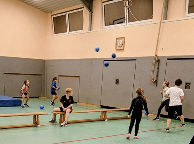 Kinder spielen mit Bällen in einer Turnhalle.