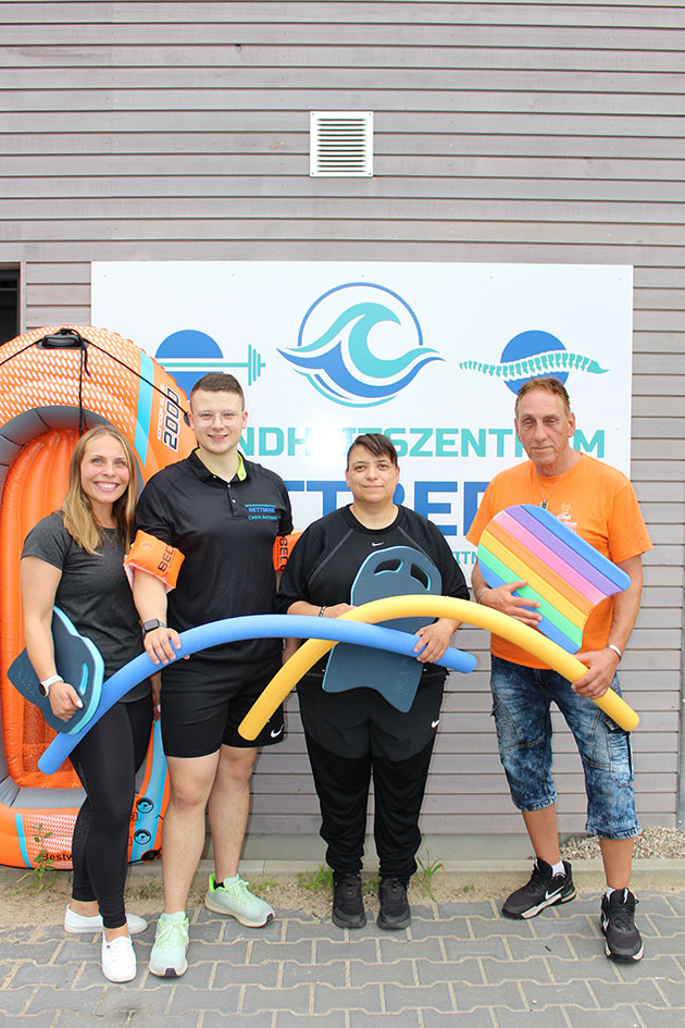 Vier Personen mit Schwimmausrüstung vor einem Schild