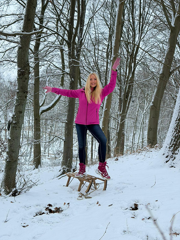 Frau balanciert auf einem Schlitten im verschneiten Wald.