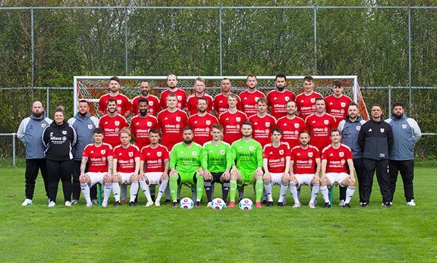 Fußballmannschaft posiert auf einem Spielfeld.
