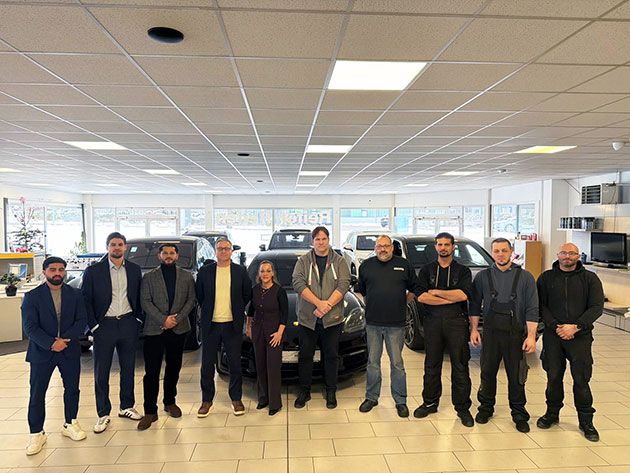 Team in einem Autohaus steht in einer Reihe vor Fahrzeugen.