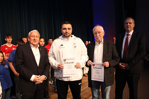 Männer stehen auf einer Bühne mit Urkunden