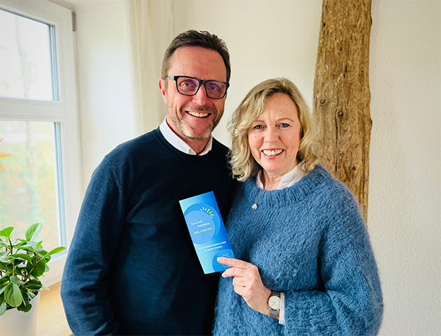 Ein Paar hält ein blaues Heft vor einem Fenster.