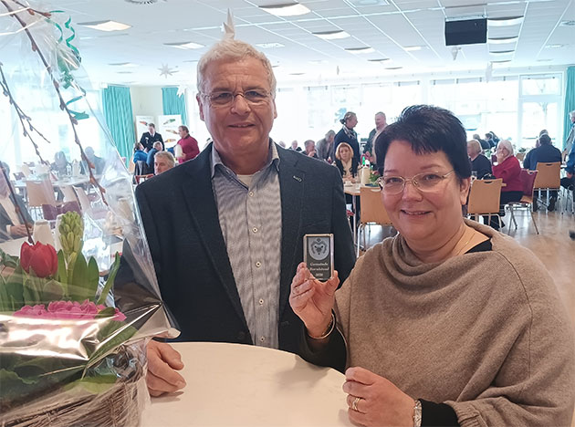 Zwei Personen halten eine Medaille in einem vollen Raum.