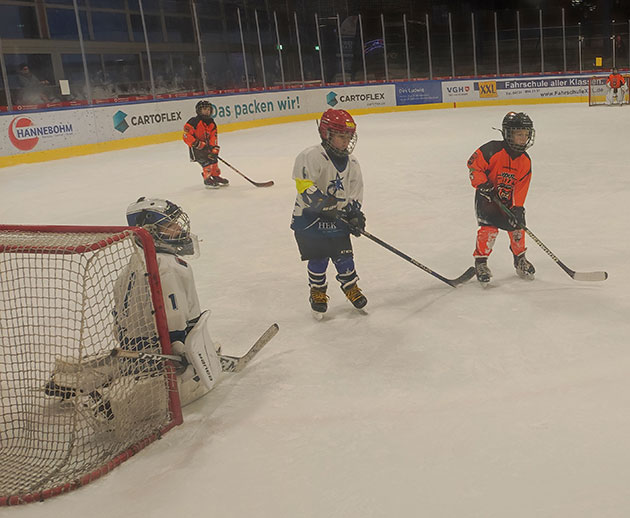 Kinder spielen Eishockey in einer Halle.