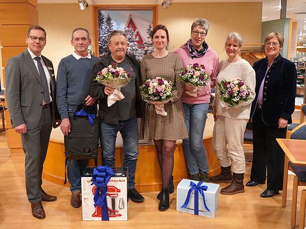 Sieben Personen posieren mit Geschenken und Blumensträußen.