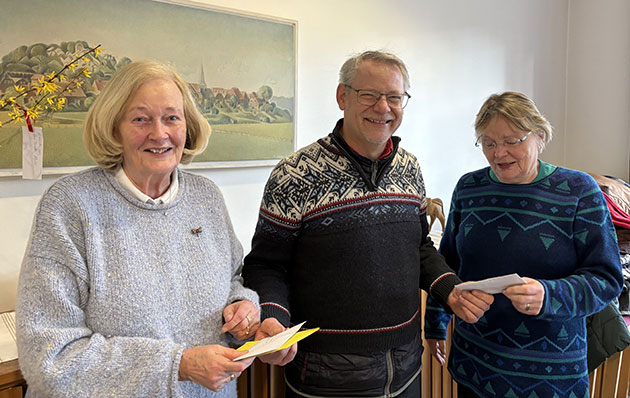 Drei Personen halten Karten in einem Raum mit Gemälde.