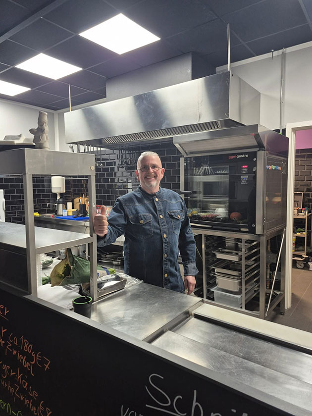 Mann in Küche zeigt Daumen hoch neben Edelstahlgeräten.