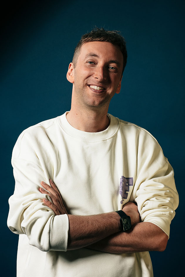 Lächelnde Person mit verschränkten Armen vor blauem Hintergrund.