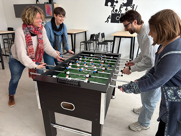 Vier Personen spielen Tischfußball in einem modernen Raum.