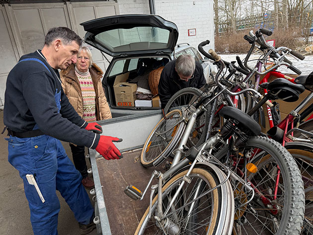 Drei Personen verladen Fahrräder auf einen Anhänger.