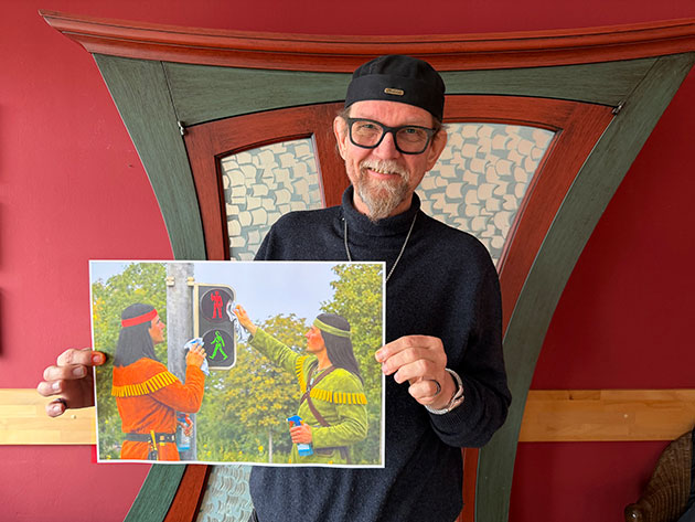 Mann hält Bild von zwei sich grüßenden Figuren an Ampel.