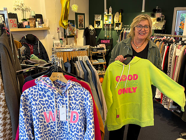 Frau in Boutique hält gelben Hoodie mit Aufschrift.