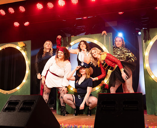 Frauen in Kostümen auf einer Bühne mit buntem Licht.