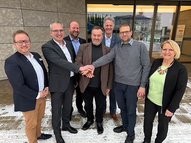 Acht lächelnde Personen stehen vor einem Gebäude.