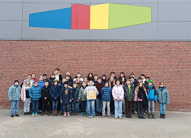 Eine Gruppe von Kindern vor einer Ziegelwand mit buntem Kunstwerk.