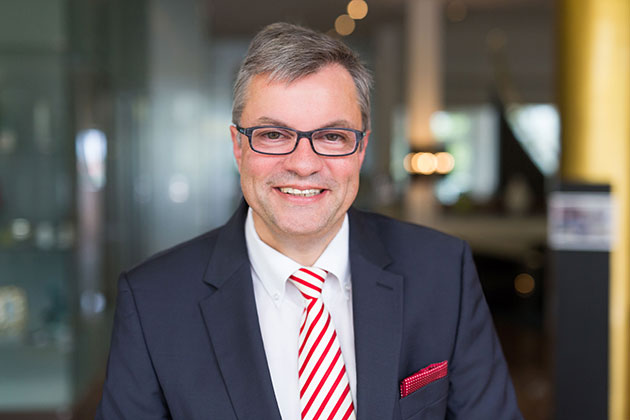 Mann in Anzug mit rot-weiß gestreifter Krawatte lächelt.