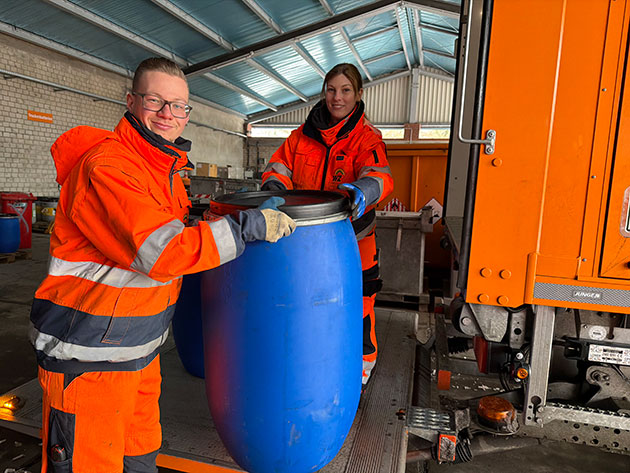 Zwei Personen in orangefarbener Kleidung mit einem blauen Fass.