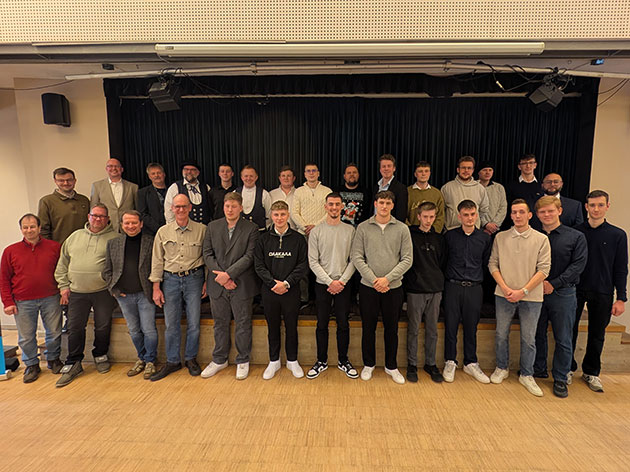 Gruppe von Menschen posiert auf einer Bühne in einem Raum.