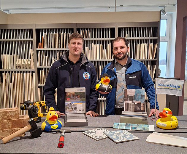Zwei Männer mit Enten und Bauwerkzeugen in einem Showroom.