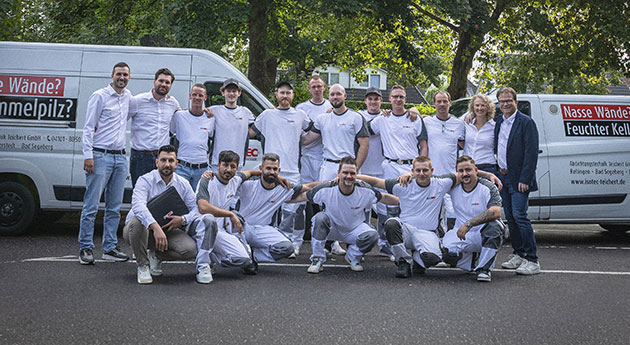 Gruppe von 16 Personen vor zwei Transportern posiert.