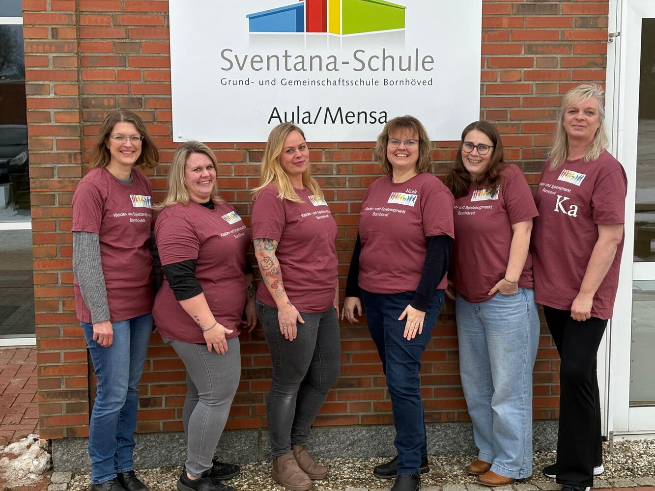 Sechs Frauen in gleichen T-Shirts vor einem Schulschild.