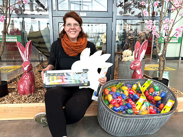 Frau hält Ostersachen, umgeben von Deko-Hasen im Geschäft.