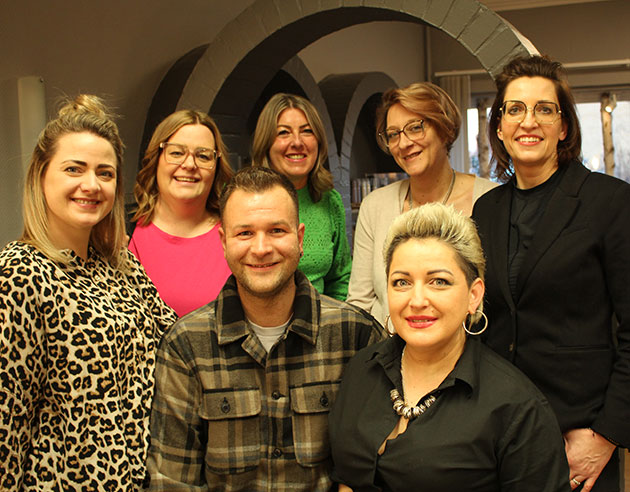 Gruppe von sieben lächelnden Menschen in einem Büro.