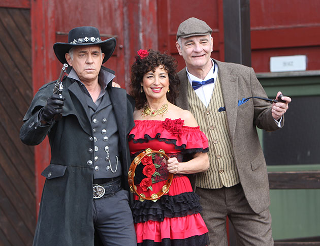 Drei Menschen in Kostümen mit Tamburin und Pistole posieren.