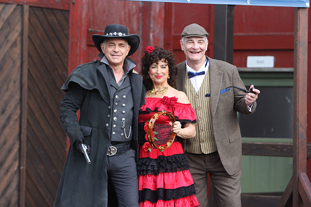 Drei Personen in Western- und Kostümkleidung posieren lächelnd.