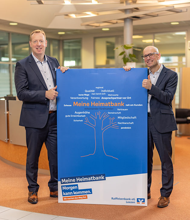 Zwei Männer halten ein blaues Plakat der Raiffeisenbank.