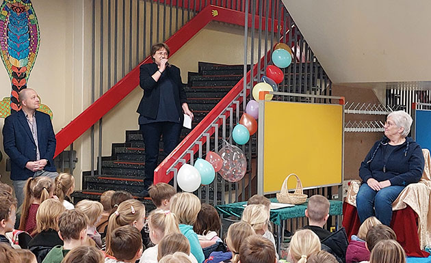 Frau spricht auf Treppe zu Schülern; bunte Luftballons sind zu sehen.