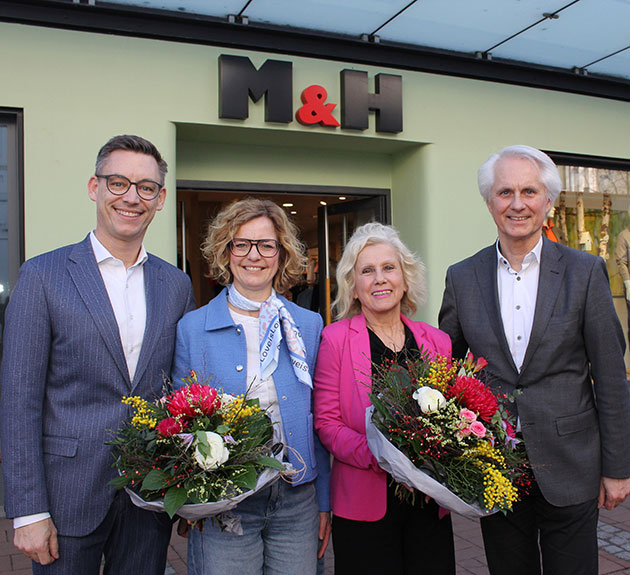 Vier Personen mit Blumensträußen vor einem Geschäft.