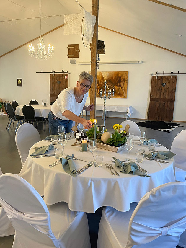 Frau dekoriert Tisch mit Kerzen und Blumen.