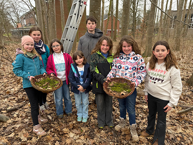 Gruppe von Kindern im Wald mit Körben voll Blätter.