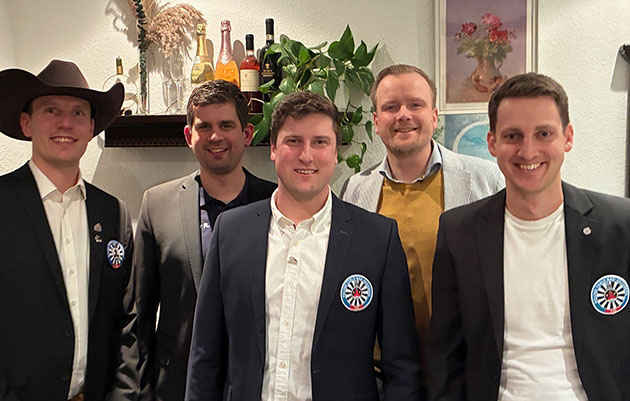 Fünf lächelnde Männer in Anzügen stehen nebeneinander.