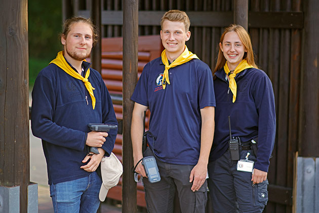 Drei junge Erwachsene mit gelben Halstüchern lächeln in die Kamera.