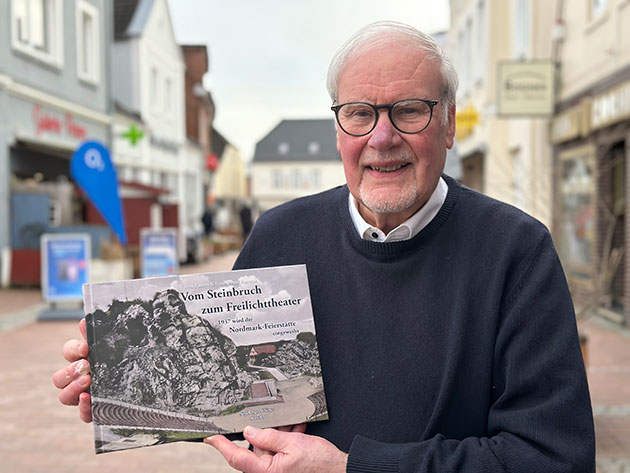 Mann hält ein Buch in einer belebten Einkaufsstraße.