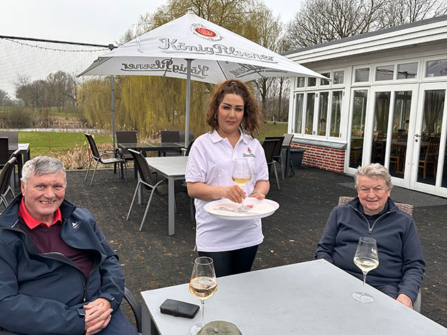 Zwei Männer und eine Frau auf einer Terrasse mit Weingläsern.