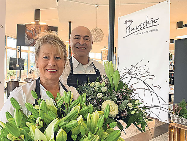 Zwei Personen mit Blumenarrangements im Restaurant Pinocchio.