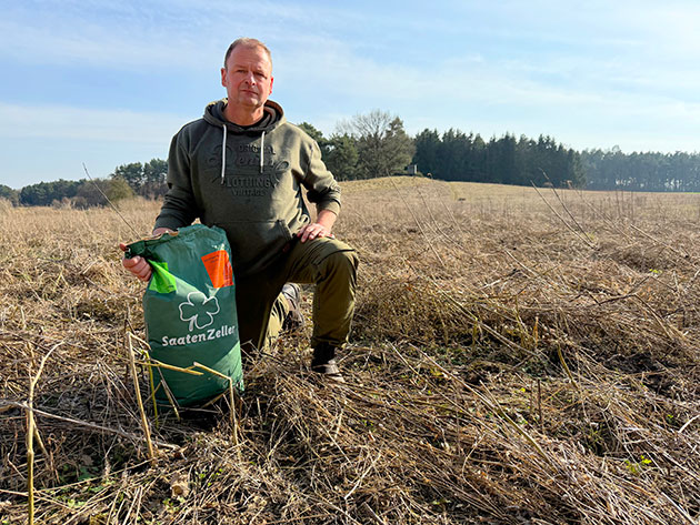 Mann kniet auf trockenem Feld mit Saatgutbeutel.