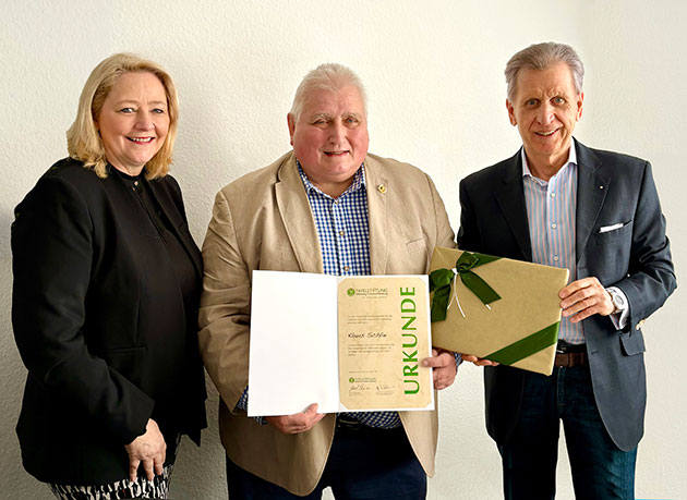 Drei Personen mit einer Urkunde und Geschenkbox.