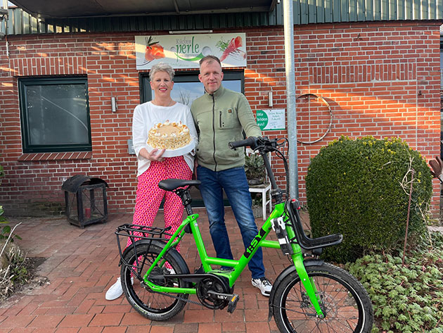 Ein Paar mit Kuchen und grünem Fahrrad vor einem Gebäude.