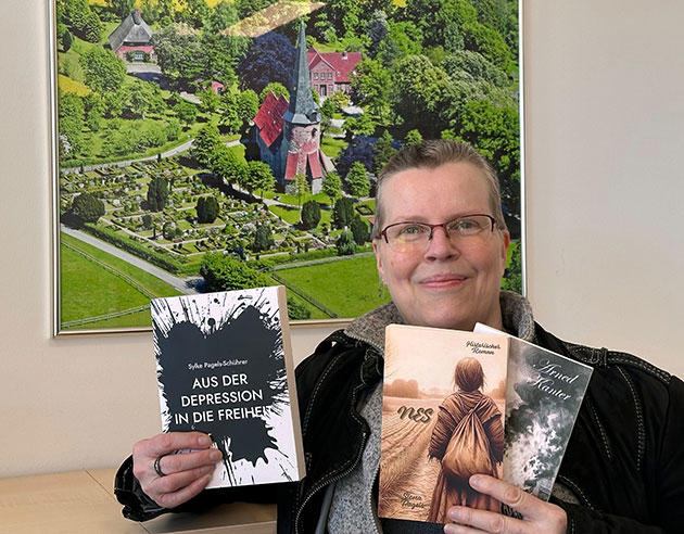 Person mit Brille hält drei Bücher vor Luftbild.