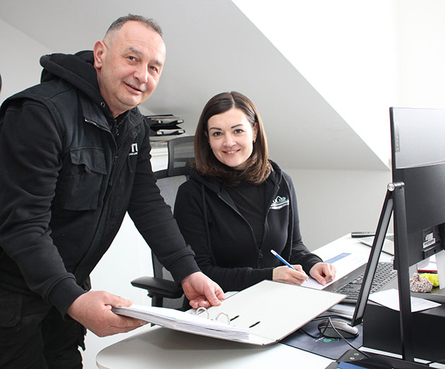 Zwei Personen im Büro mit Datenordner am Schreibtisch.