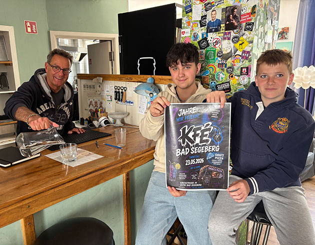 Drei Personen in einem Café mit Festivalposter.