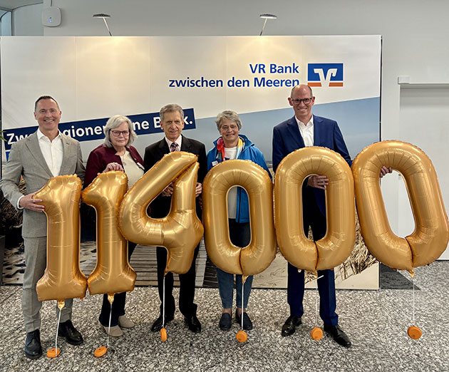 Fünf Personen halten goldene Zahlenballons: 114000.