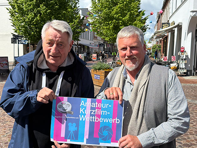 Zwei Männer halten ein Plakat für einen Kurzfilmwettbewerb.