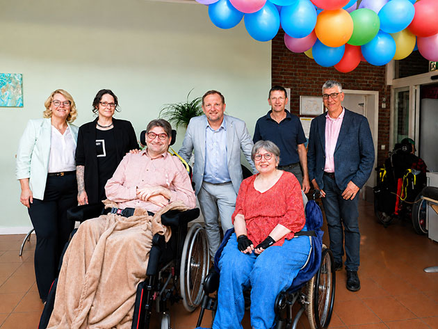 Gruppe posiert unter bunten Luftballons in einem Raum.